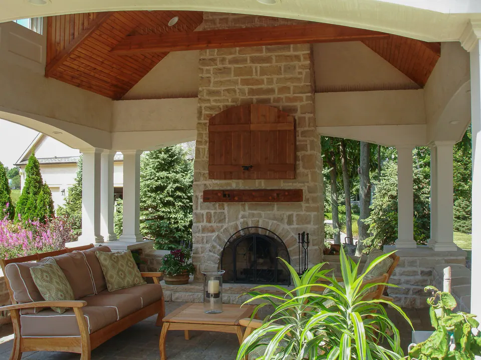 Outdoor pavilion fireplace with natural stone chimney, brick firebox, stone hearth, wood ceiling, and covered seating
